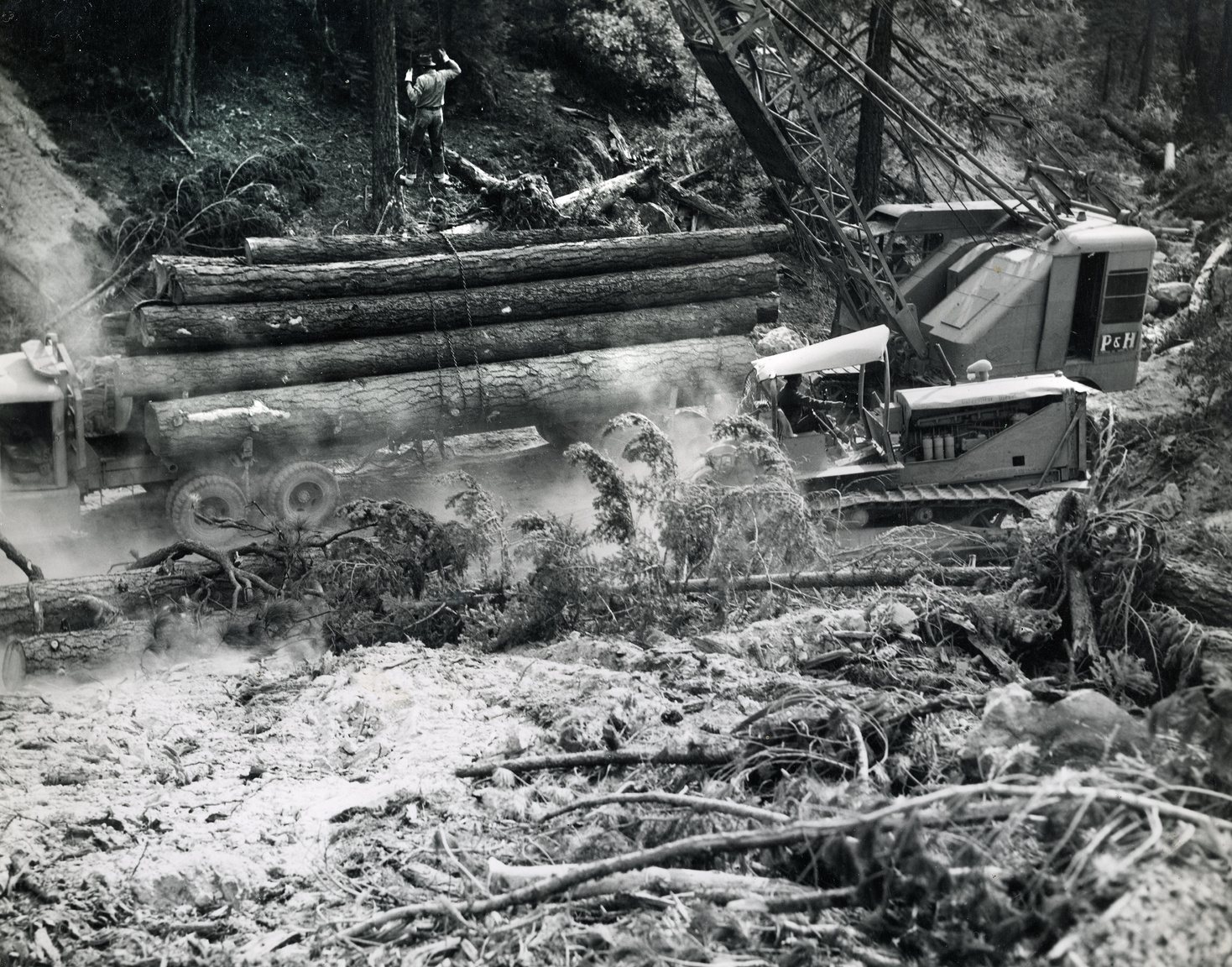 Crane and log truck yarding timber on a dusty forest road, circa 1950