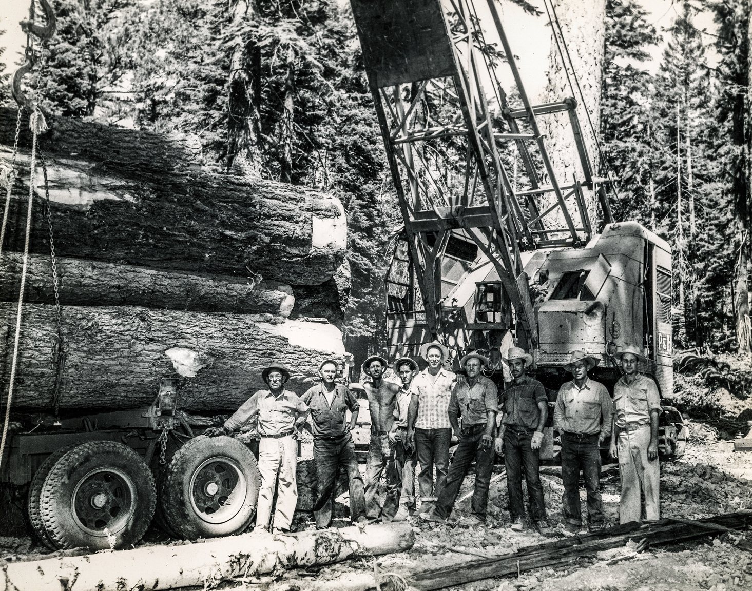 Logging crew of nine men standing beside a loaded log truck and a P&H crane, circa 1950